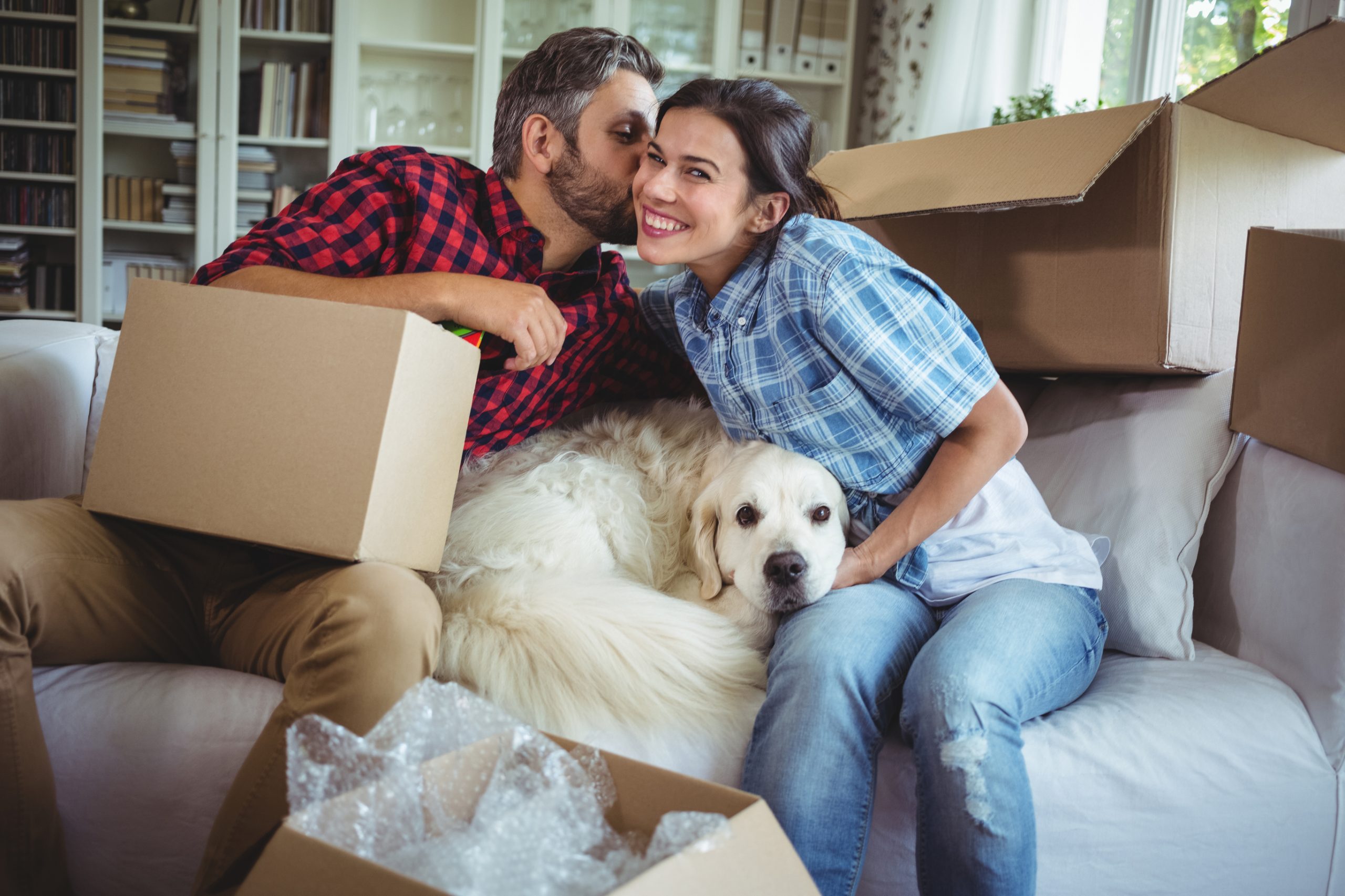 Happy couple unpacking boxes and kissing with dog between them